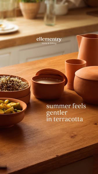 This ad showcases a variety of terracotta dishes on a wooden table with the text overlay 'summer feels gentler in te