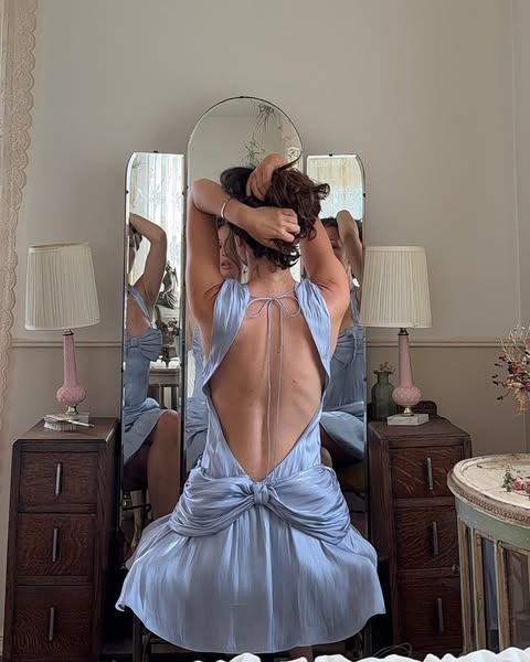 This image ad features a woman in a light blue dress, facing a vintage vanity mirror. She is in the process of styling h