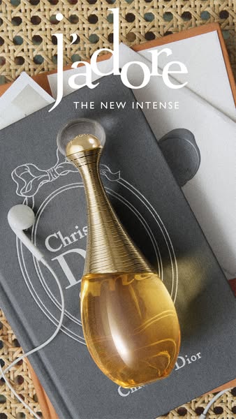 The ad features J'adore THE NEW INTENSE perfume by Dior sitting on top of a book with white earbuds. The scene creat