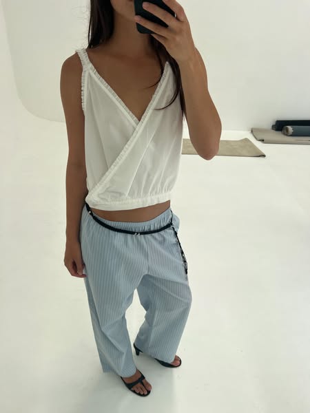An ad showcasing light blue and white striped pants. The image features a woman in a white wrap top and the pants, holdi