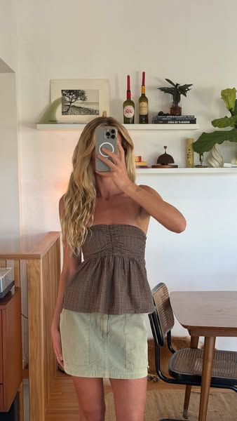 This ad features a woman holding her phone up to the mirror, taking a photo of herself while wearing a brown and tan str