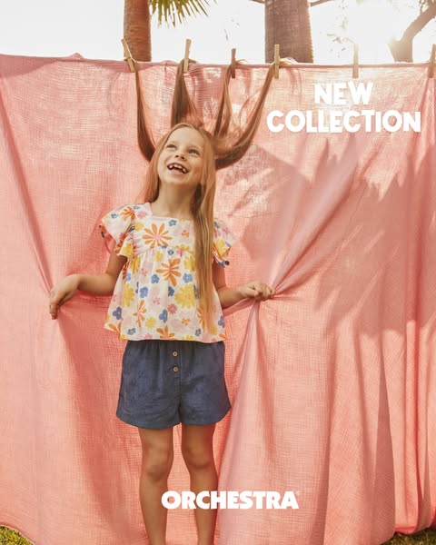 An ad for Orchestra clothing features a smiling girl in a floral top and denim shorts standing in front of a blush pink 