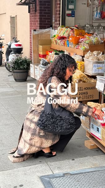 This ad features a lifestyle shot of a woman in a patterned coat crouching in front of a storefront, holding a black ruf