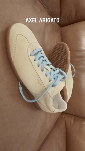 A static image ad displaying a pair of Axel Arigato sneakers on a couch.