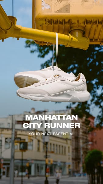 This image ad showcases a pair of white Manhattan City Runner sneakers hanging from a traffic light in what appears to b