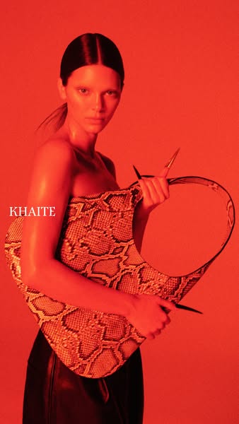The ad features a high fashion snakeskin print bag. A model is holding the Khaite bag in front of a red background. The 