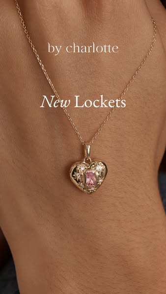 Close up of a gold heart locket with a pink gemstone on a gold chain, worn by a woman, for the 'by charlotte' br
