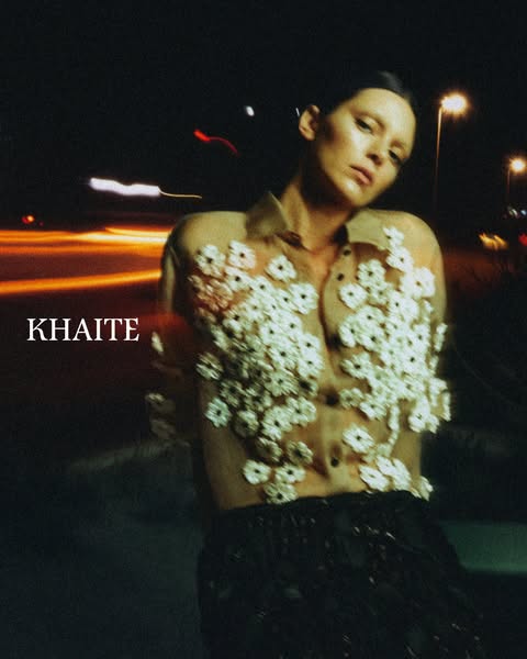 This ad for Khaite features a woman in one of their sheer, floral-applique blouses in an urban outdoor nighttime setting