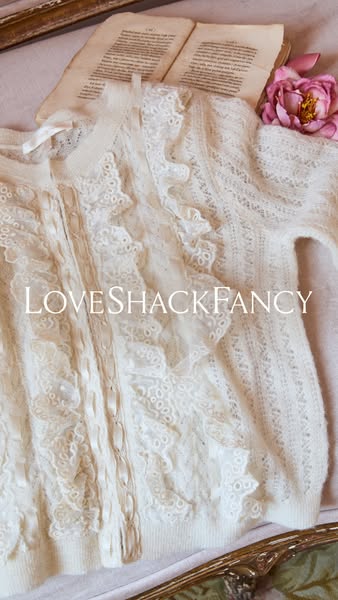 An ad featuring a LoveShackFancy sweater next to a flower and a book, all sitting on a vintage-looking fabric.