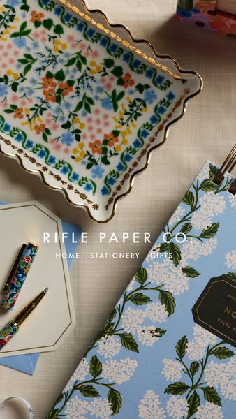 This ad showcases a variety of Rifle Paper Co. products, including a floral tray, a floral pen, a floral notebook, and s