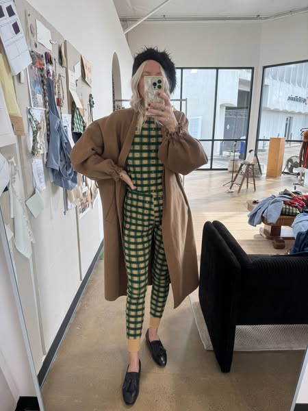 A full-length mirror selfie of a person wearing a green and beige plaid outfit with a brown coat. The ad showcases the o