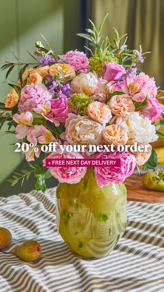 This image ad features a lush flower arrangement in a speckled green vase, set against a striped tablecloth. The ad prom