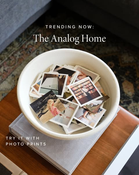A lifestyle image showing a bowl of photos on top of a photo album on a wooden table with a gray couch in the background