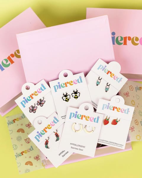The image showcases a variety of earrings by Pierced Co. displayed on their packaging. The products are arranged to high