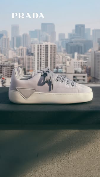 This image ad displays a Prada sneaker against a blurred city skyline, emphasizing the brand's high-end urban style.