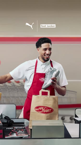 An employee at Hali Mart is wearing a Puma t-shirt, red apron, and is holding up a shoe from Puma. A bag from Hali Mart 