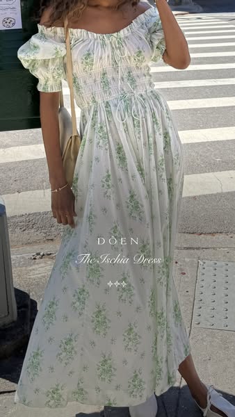 This image ad for DÔEN features a woman wearing the 'Ischia Dress' while walking outdoors. The ad presents the d
