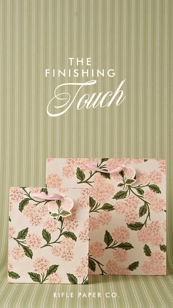 This ad features two floral Rifle Paper Co. gift bags against a sage green striped background. The image promotes the br