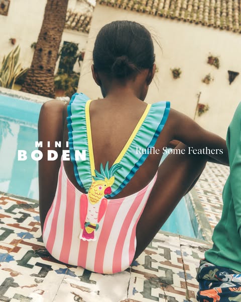This image ad for Mini Boden features a child wearing a striped swimsuit with a cartoon parrot design, positioned by a p