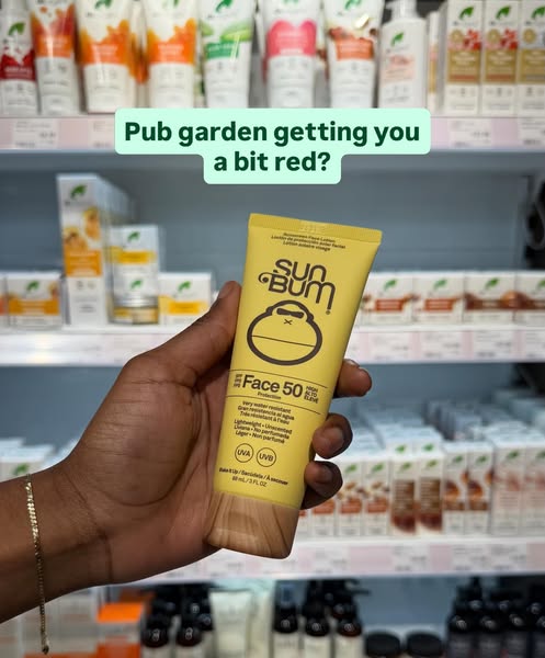 This image ad for Sun Bum sunscreen features a tube of Face 50 sunscreen being held up against a backdrop of store shelv
