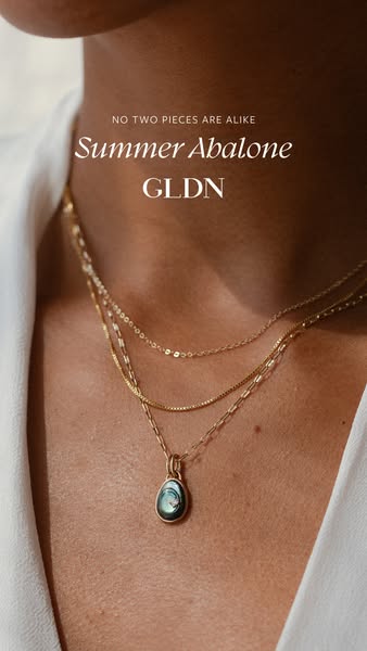 This ad showcases a stack of three delicate, gold necklaces, one of which features an abalone pendant.