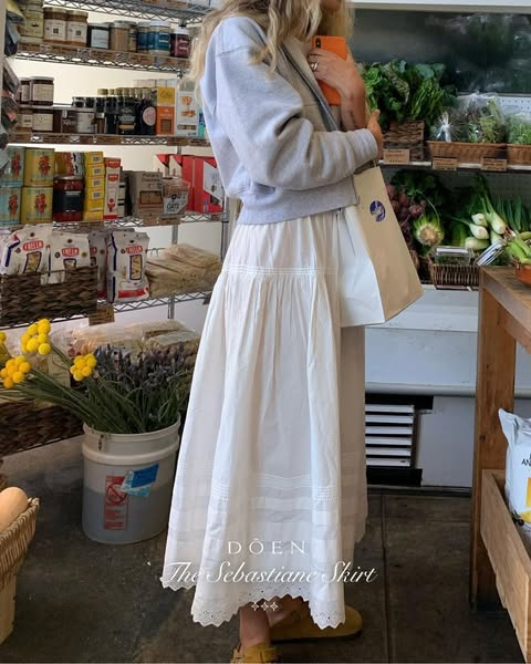 This image ad is focused on the Doen Sebastiane Skirt. The ad features a woman in a grey sweatshirt and a white Doen ski