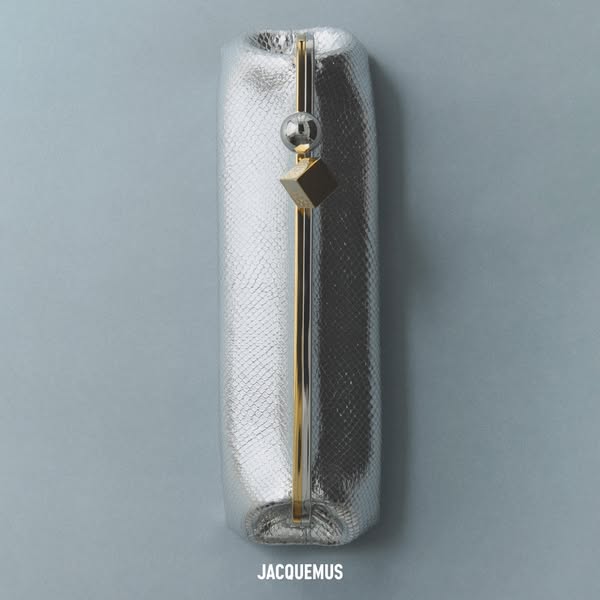 This ad showcases a silver clutch with a snake skin texture. The clutch has a gold clasp and a silver ball and gold cube