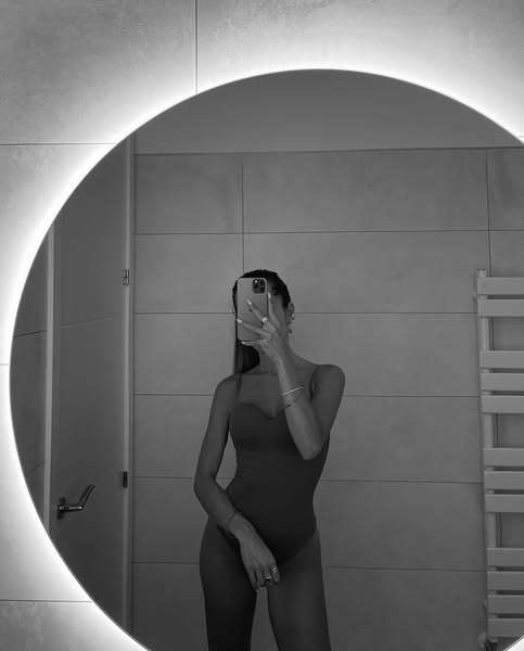 This ad features a woman in a bodysuit taking a mirror selfie in a bathroom with a round mirror. The ad is likely for th