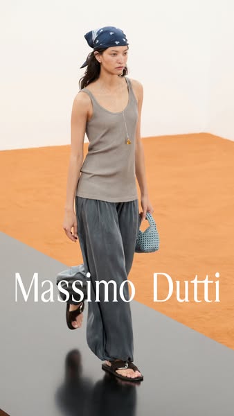 This ad features a woman walking on a black runway, wearing Massimo Dutti clothing and accessories. The background is or