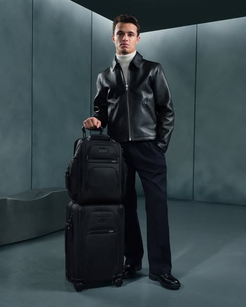 Image showcasing a man in fashionable clothing next to Tumi luggage, showcasing a backpack stacked atop a rolling suitca