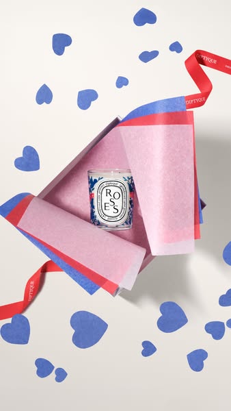 An overhead shot focuses on a Diptyque Roses candle nestled in an opened gift box with tissue paper and a branded ribbon