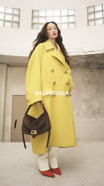 This ad features a woman wearing a yellow Balenciaga coat and carrying a brown Balenciaga bag, set in a bright, modern s