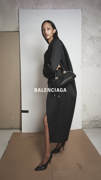 This ad features a high-fashion model showcasing a Balenciaga handbag. She is wearing a black dress and heels. The backg