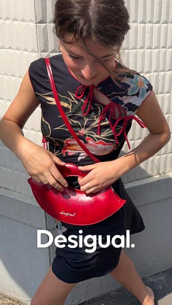 This is a product display ad featuring a woman holding a red handbag. The focus is on the Desigual brand, with the brand