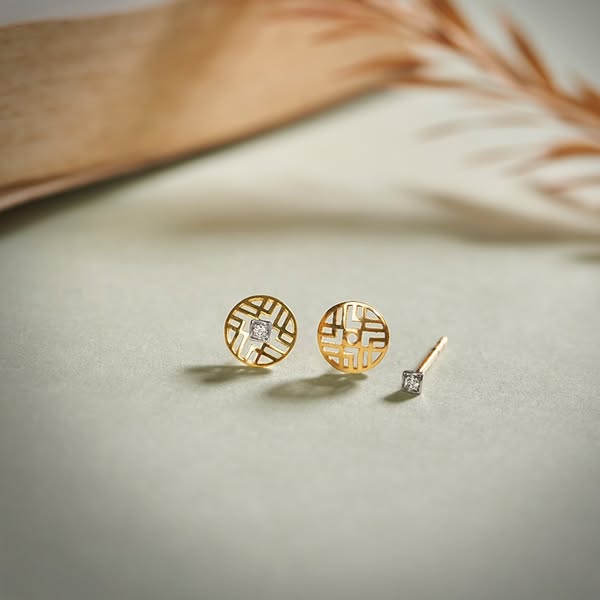 This ad showcases a pair of gold earrings with a diamond stud. The earrings are displayed on a neutral surface with a bl