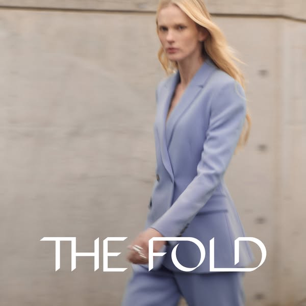 This ad features a woman wearing a light blue pantsuit, showcasing the brand 'The Fold'. The visual style is cle