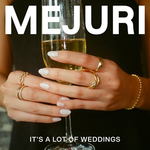 An image ad for Mejuri jewelry featuring a woman holding a champagne flute with various gold rings and a bracelet on her