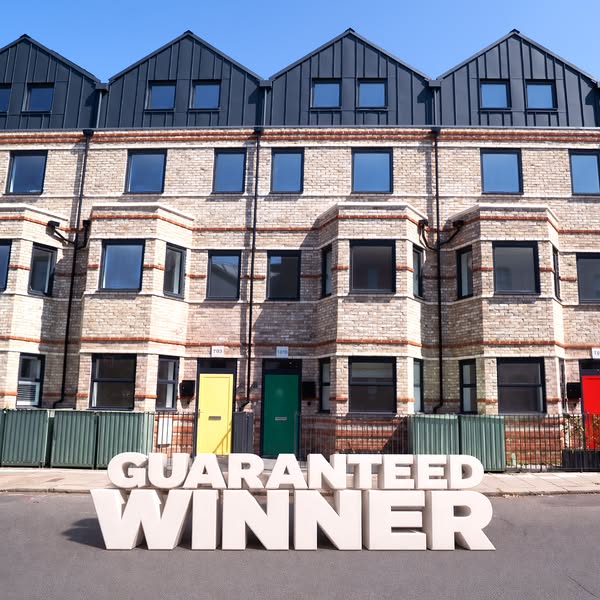 This image shows a row of terraced houses with brightly colored front doors. The words "GUARANTEED WINNER" are