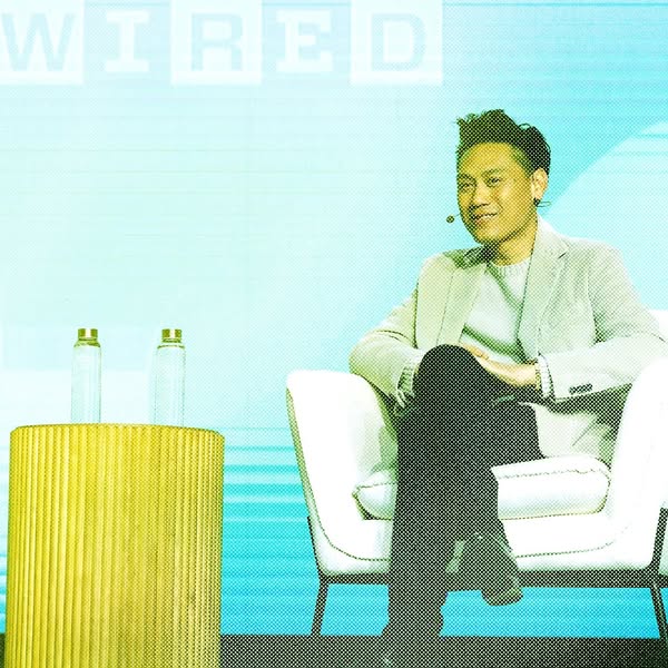 This ad features a man sitting in a chair on stage at a WIRED event. There are two glass water bottles on a table next t