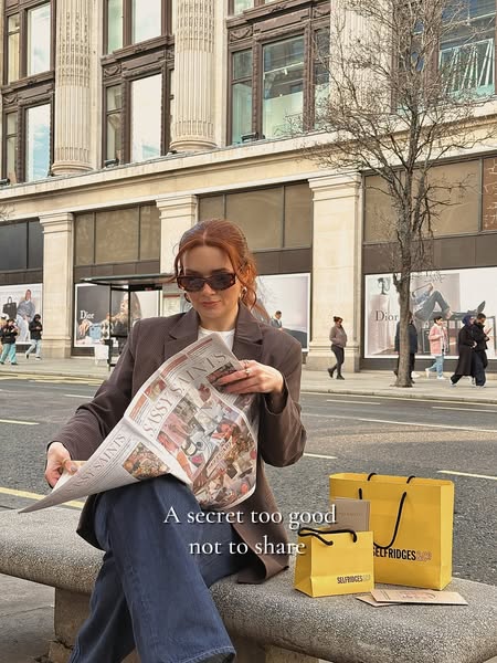 The image ad features a woman sitting on a bench in front of Selfridges, reading a newspaper, and accompanied by two Sel