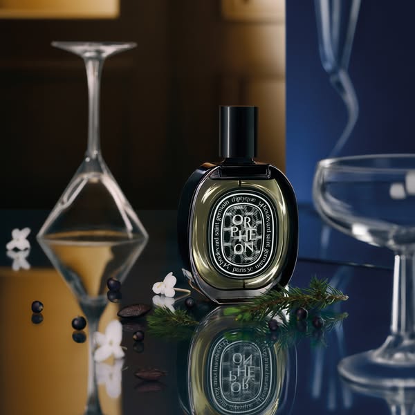 This image ad showcases the Diptyque Orphéon perfume bottle in a lifestyle setting. The product is positioned amidst coc