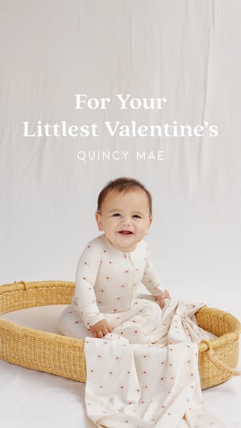 This image ad for Quincy Mae features a baby wearing a long-sleeved romper with a heart pattern, sitting in a woven bask