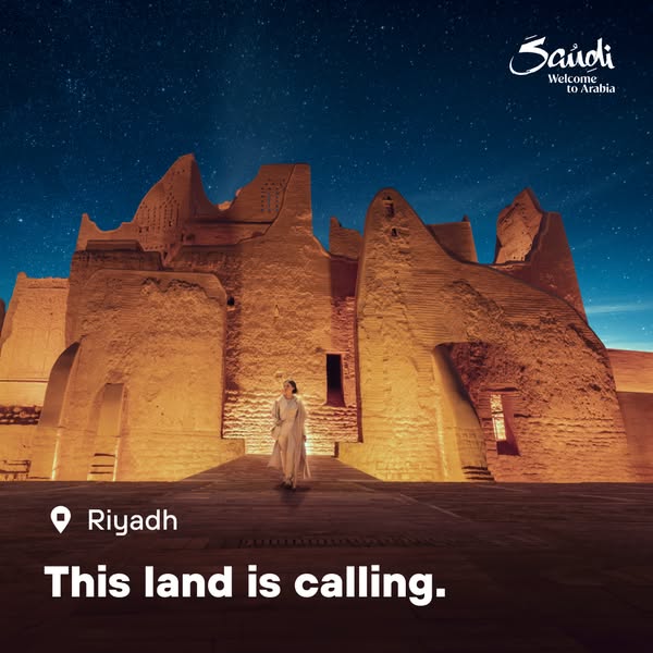 This image ad for Saudi Arabia tourism features a woman walking toward a large, sand-colored building under a starry sky
