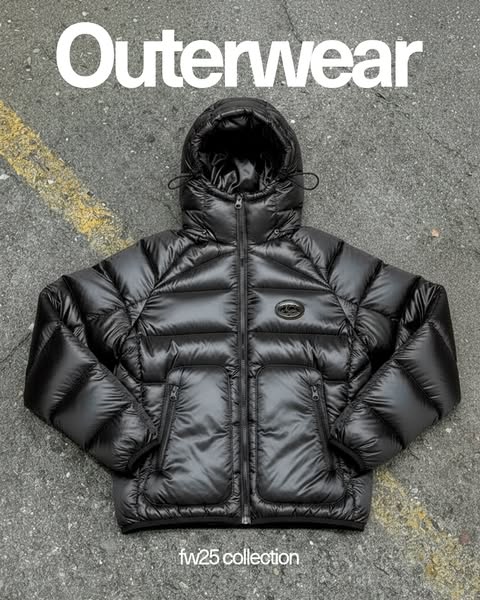 This ad showcases a black puffer jacket from the fw25 collection. The jacket is displayed against a concrete background,