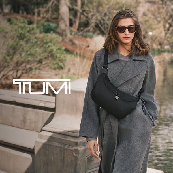 An image ad shows a woman walking outside while wearing a black Tumi bag across her chest.