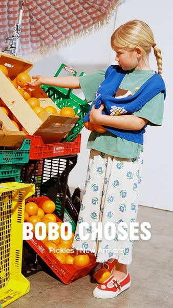 A lifestyle image ad showcasing a young girl wearing a green t-shirt, floral print pants, and red shoes while reaching f