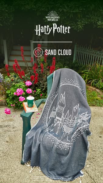 This ad showcases a Harry Potter-themed towel from Sand Cloud, displayed outdoors on a chair with a book and a drink.