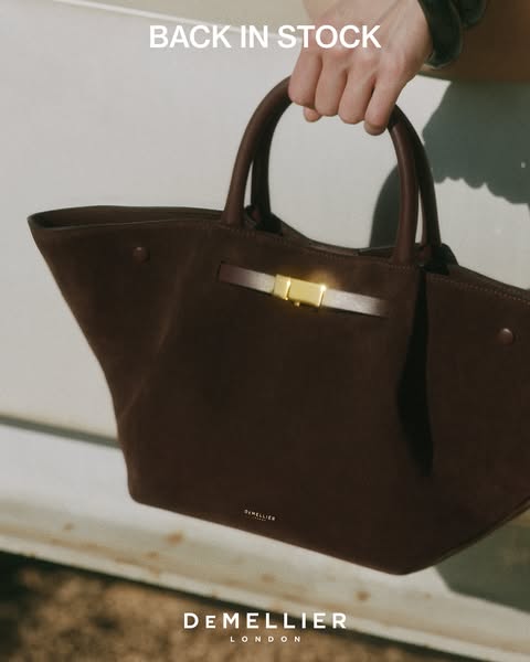 This image ad showcases a single brown DeMellier London handbag. The text overlay on the image reads "BACK IN STOCK