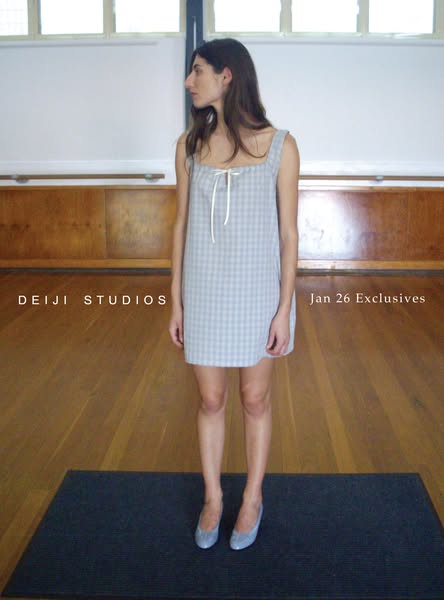 This ad features a woman modeling a short gray and white gingham dress from Deiji Studios to promote their Jan 26 Exclus