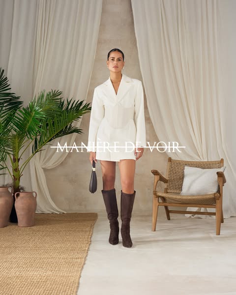 The ad showcases a woman in a white blazer dress, knee-high boots, and a small handbag against a neutral backdrop with s